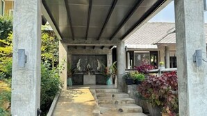 Un espacio al aire libre cubierto con una escalera de piedra que lleva a una puerta, rodeado de plantas en macetas y follaje.