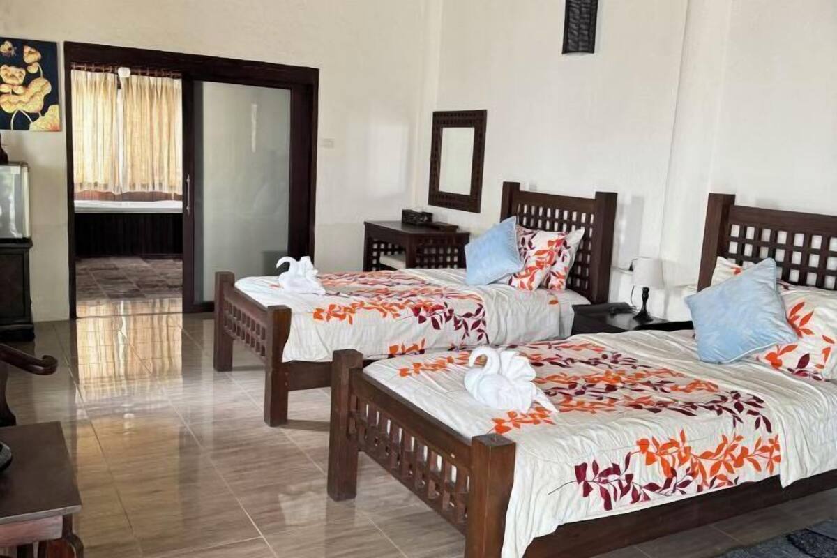 A hotel room with two wooden beds, a desk, a chair, a mirror, and a door leading to another room.