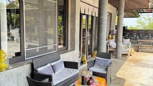 Un espacio de estar al aire libre cubierto con mobiliario de mimbre, ventanas amplias y vistas del paisaje circundante.