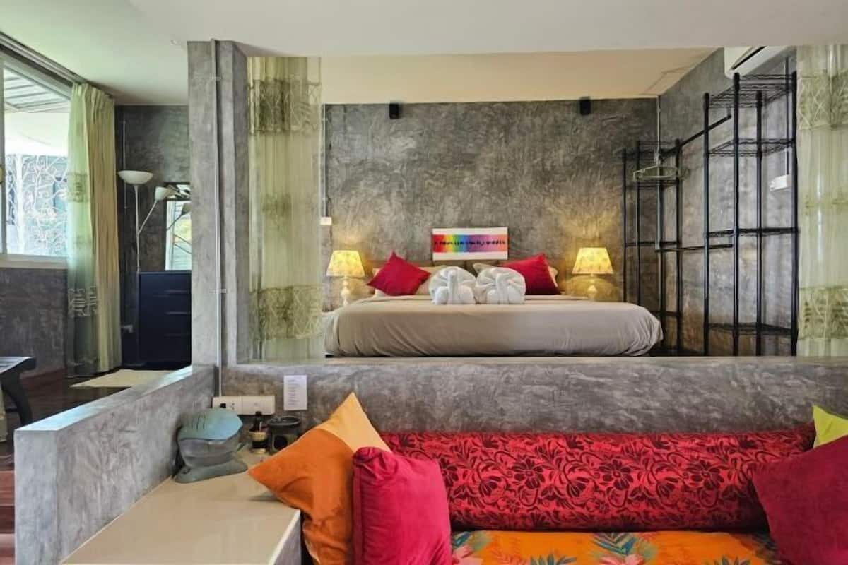 A bedroom with a bed, two bedside lamps, a nightstand, a sofa, and a decorative wall piece.