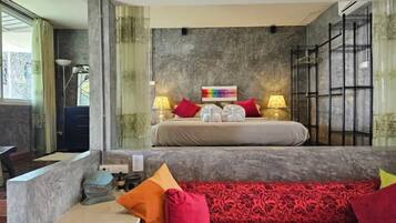 Quarto com cama, duas luminárias de cabeceira, mesa de cabeceira, sofá e um objeto decorativo na parede.