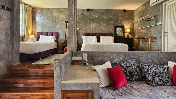 Habitación de hotel con dos camas, un sofá, una escalera de madera y una pared de piedra.