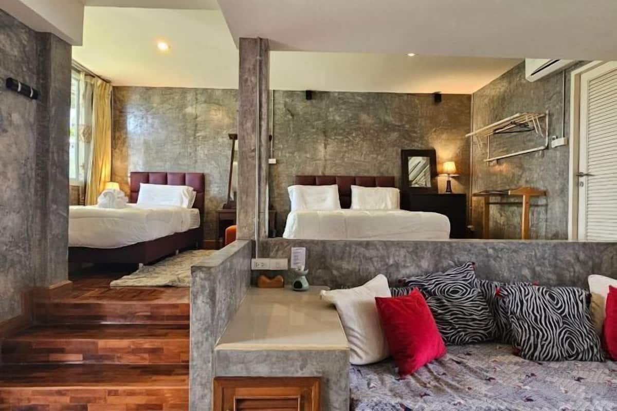 A hotel room with two beds, a sofa, a wooden staircase, and a stone wall.