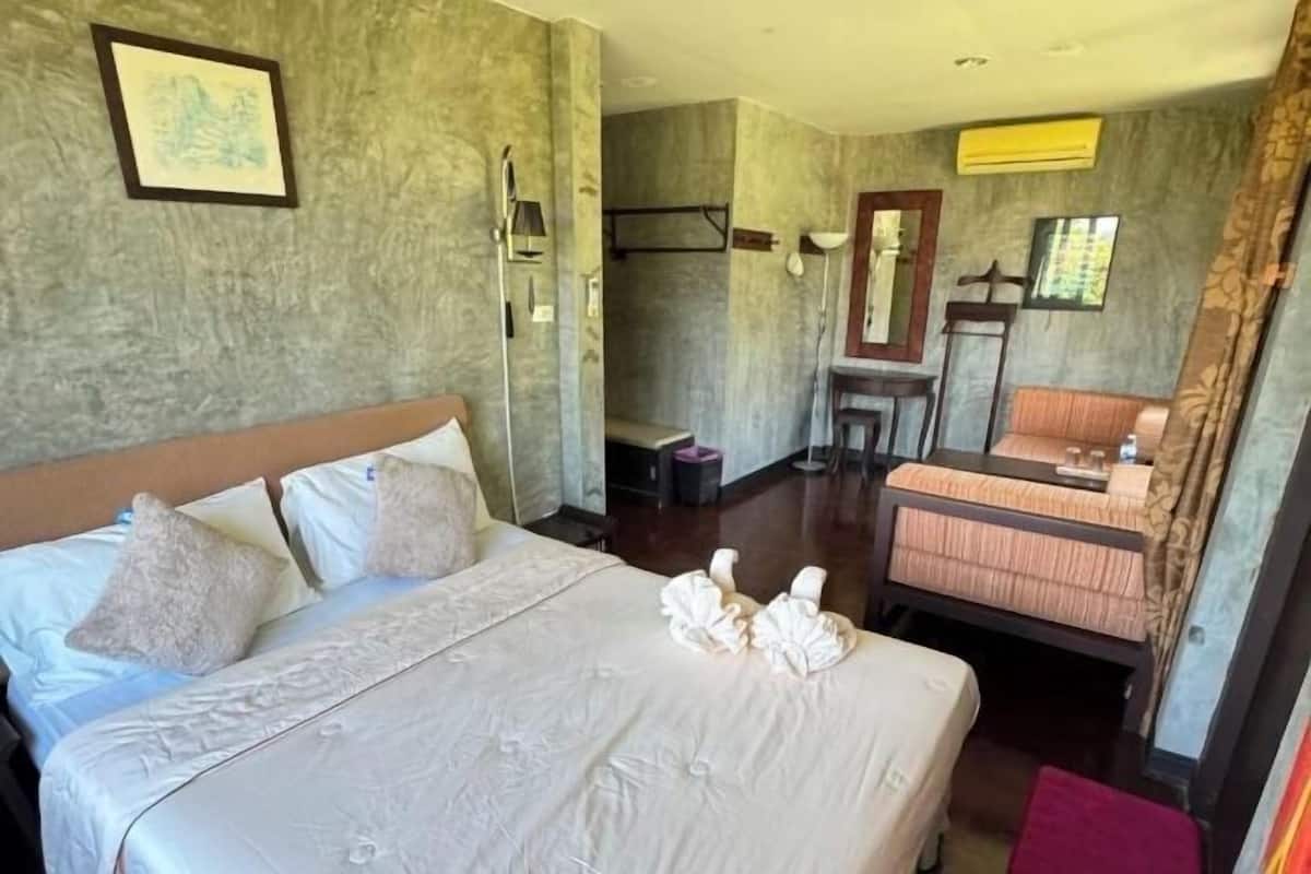 A hotel room with a large bed, a small table, a chair, and a mirror.