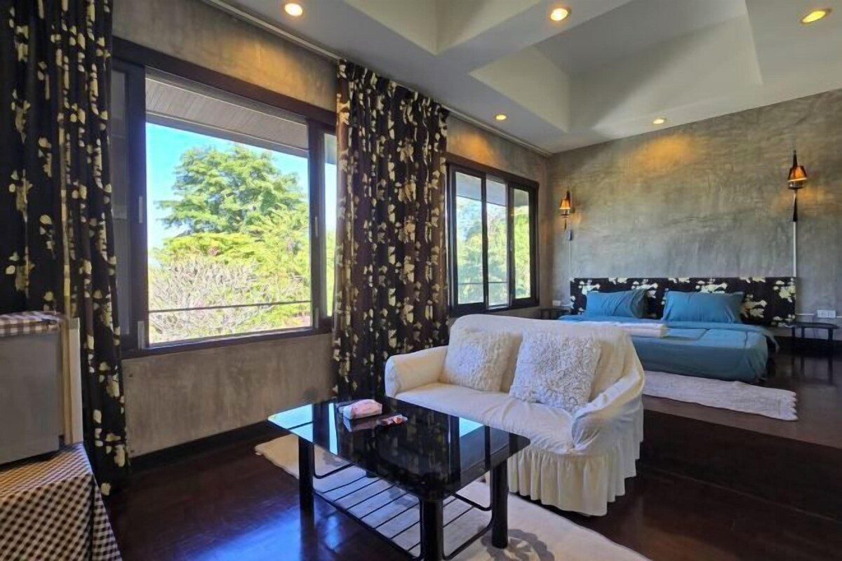 A modern living room with a sofa, a glass coffee table, and a bed with blue bedding.