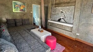 Una sala de estar moderna con un sofá, una mesita, un reposapiés rosa, un cuadro y una ventana con vistas.