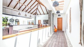A modern kitchen with a wooden ceiling, a long counter, and hanging pendant lights. - Canggu CAROLE · (Bali)