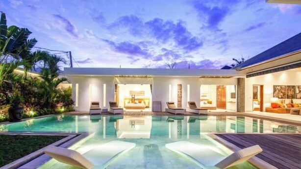 A modern outdoor pool area with lounge chairs and a well-lit interior space. - Canggu CAROLE · (Bali)