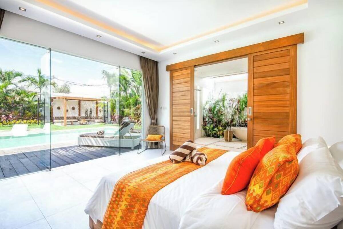 A modern bedroom with a large bed, a sliding glass door to a pool area, and a view of the outdoors.