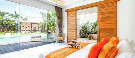 A modern bedroom with a large bed, a sliding glass door to a pool area, and a view of the outdoors.