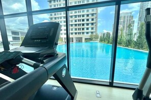 A treadmill in a room with large windows overlooking a swimming pool and high-rise buildings. - EduStay Lofts - Cyber University Circle (Cyberjaya)