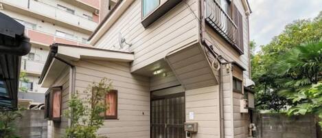 A residential building with a sloped roof, a gated entrance, and a small garden area.