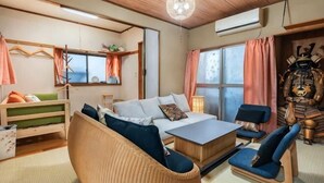 Une pièce comprenant un lit, deux chaises, un canapé, un luminaire suspendu, une fenêtre avec des rideaux, une étagère fixée au mur et une statue décorative.