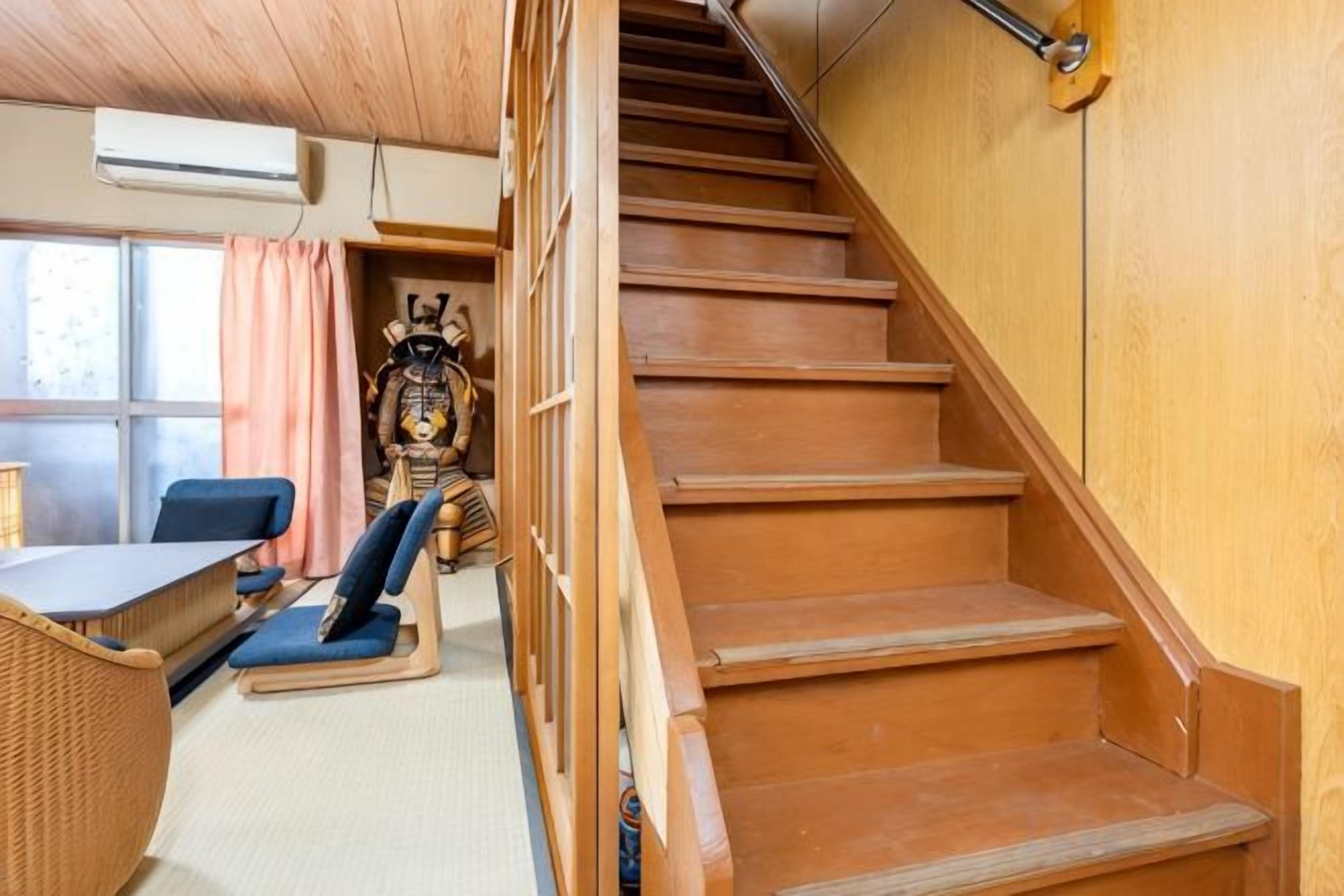 A wooden staircase leading to a room with a tatami mat floor, a traditional Japanese chair, and a table.
