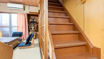 A wooden staircase leading to a room with a tatami mat floor, a traditional Japanese chair, and a table.