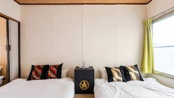 A hotel room with two beds, a wooden ceiling, a window with curtains, and a wall-mounted lamp.