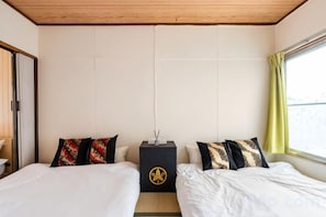 A hotel room with two beds, a wooden ceiling, a window with curtains, and a wall-mounted lamp. - Yotsugi2 House (Tokyo)