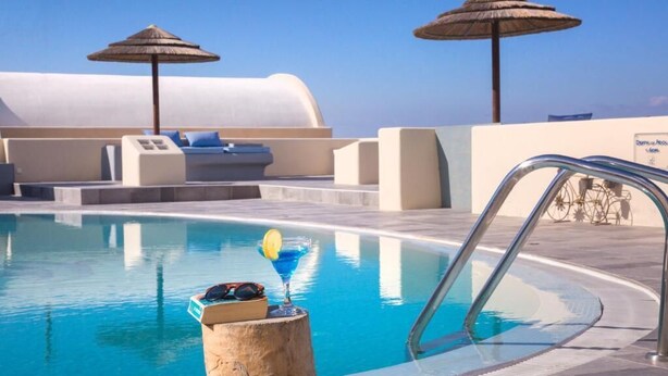 Un área de piscina con sillas de descanso y sombrillas, un poste de madera con una bebida, y un letrero que indica un espacio de spa.