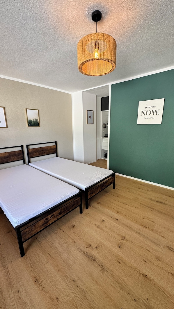 A room with two beds, a hanging light fixture, a green accent wall, and a framed motivational quote.