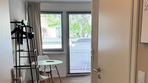 Un couloir menant à un balcon agrémenté d’une table et de chaises, d’un porte-manteau et d’une porte avec un interrupteur.