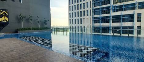 A rooftop pool with a wooden deck and a view of high-rise buildings.