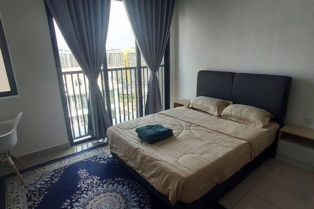 A bedroom with a bed, curtains, a chair, and a view of buildings outside.