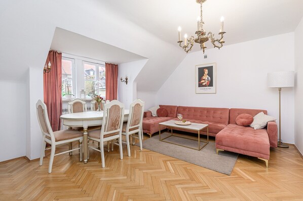 A modern living room with a dining area, a pink sofa, a chandelier, and a painting on the wall.