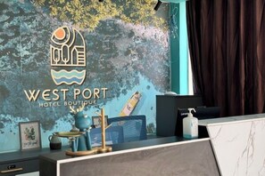 A reception desk at West Port Hotel Boutique with a logo, a framed picture, a vase, and a bottle of hand sanitizer. - Westport Hotel Boutique (Sihanoukville)