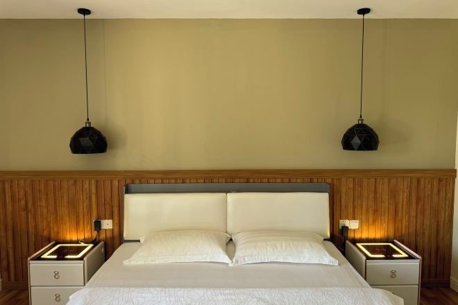 Une chambre d’hôtel avec un grand lit, deux tables de chevet et deux lampes suspendues.