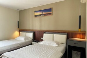 A hotel room with two beds, a nightstand, a desk, a chair, a painting of the Eiffel Tower, and a hanging light fixture. - Westport Hotel Boutique (Sihanoukville)