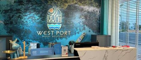 A hotel reception desk with a logo, a marble counter, and a window with blinds.