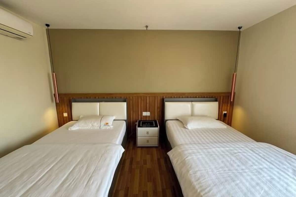 A hotel room with two single beds, wooden headboards, a nightstand with a lamp, and a wooden floor.