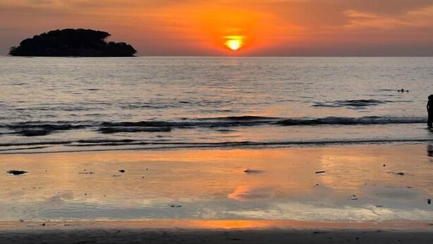Un atardecer sobre un mar tranquilo con una pequeña isla a lo lejos.