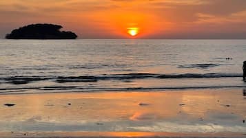 A sunset over a calm sea with a distant island and a beach in the foreground.