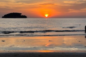 A sunset over a calm sea with a distant island and a beach in the foreground. - Westport Hotel Boutique (Sihanoukville)