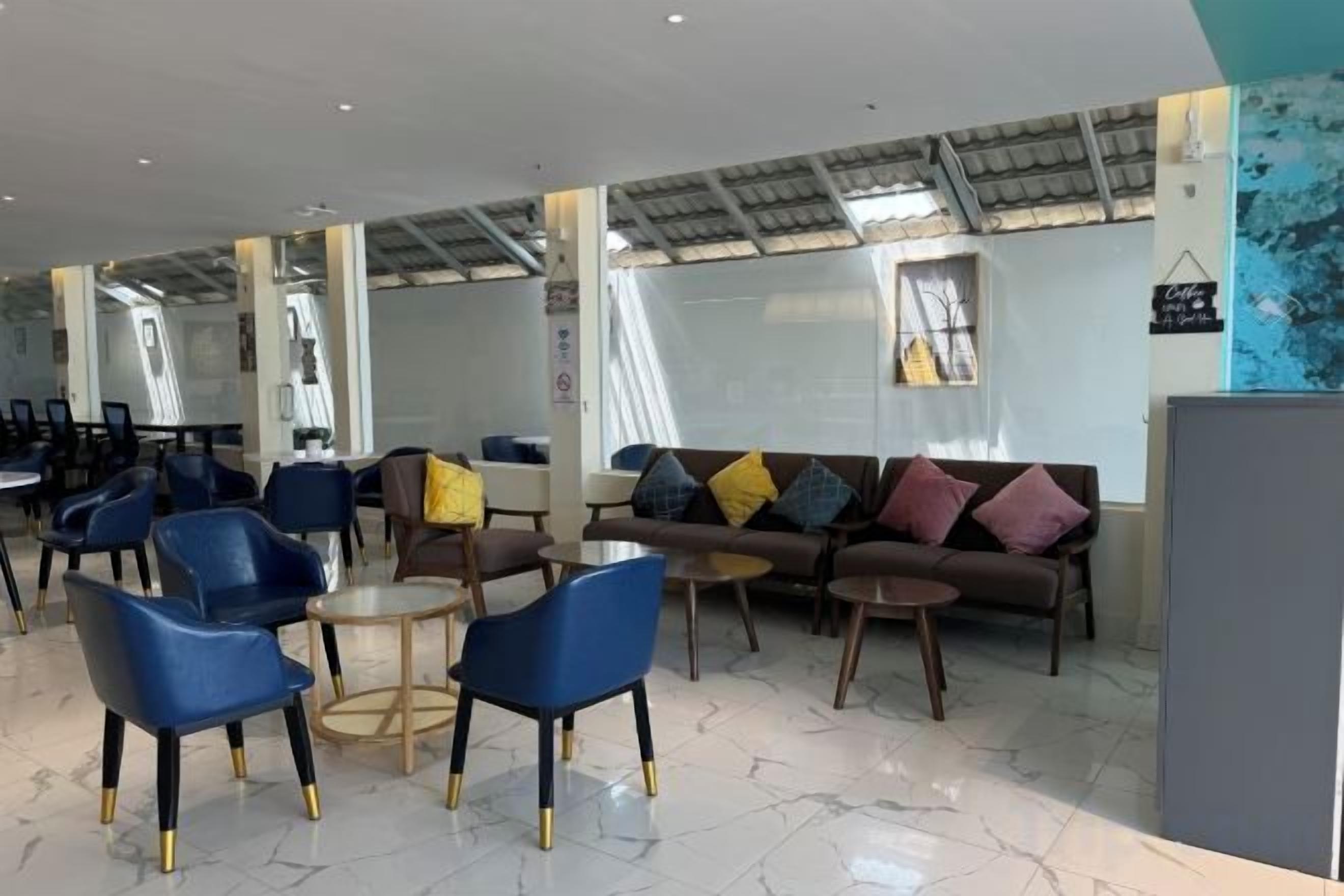 A modern lounge area with seating arrangements, including sofas and chairs, and a high ceiling with skylights.