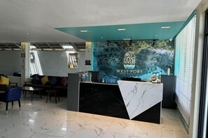 A hotel reception area with a marble counter, a sofa with colorful cushions, and a large window providing natural light. - Westport Hotel Boutique (Sihanoukville)