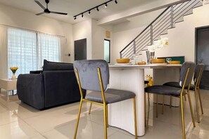 A modern living room with a sofa, a dining area with chairs, a kitchen counter, and a staircase. - Corner House Puchong 18 pax BBQ Kid Friendly (Puchong)
