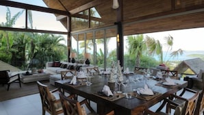 A spacious dining area with a large table set for a meal, surrounded by wooden chairs. - Purana Residence (Koh Samui)