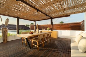 Eine Terrasse im Freien mit einem Holztisch und Stühlen, einer Couch und Blick auf die Landschaft.