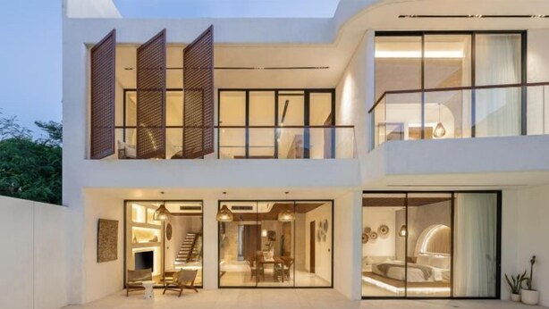 Une maison moderne à deux étages, dotée d’une piscine, de grandes portes vitrées et d’un balcon.