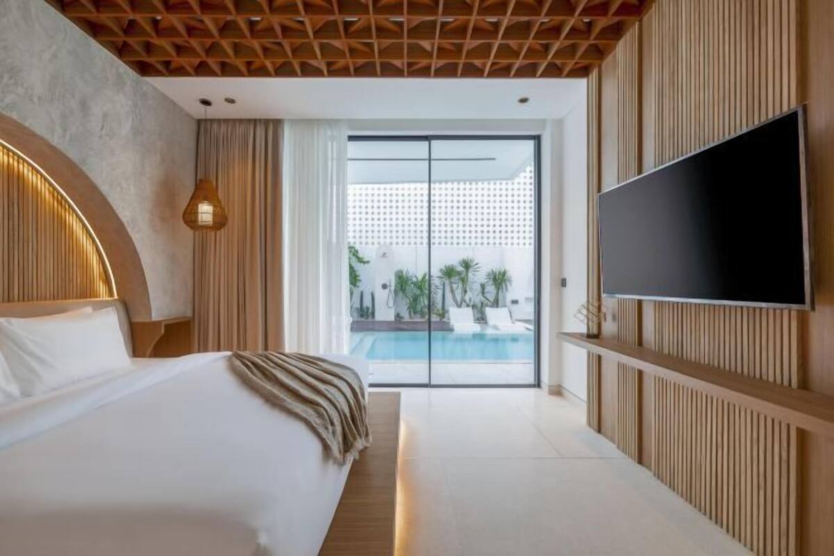 Ein modernes Hotelzimmer mit Bett, Fernseher, Blick auf den Pool und einer Holzbalkendecke.