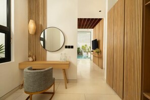 A hallway with a wooden desk, a chair, a round mirror, and a television on a wall. - Fenta Villa Canggu by Nakula (Bali)