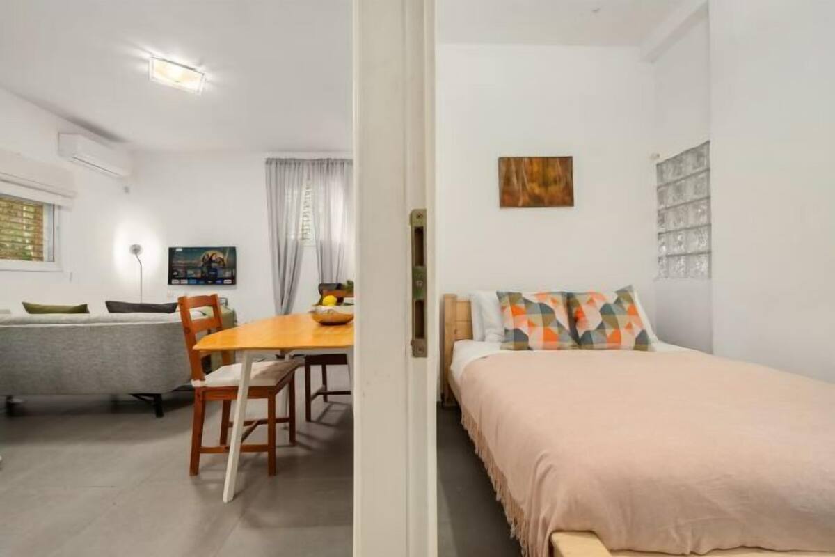 A room with a bed, a table with chairs, a sofa, a TV, and a painting on the wall.
