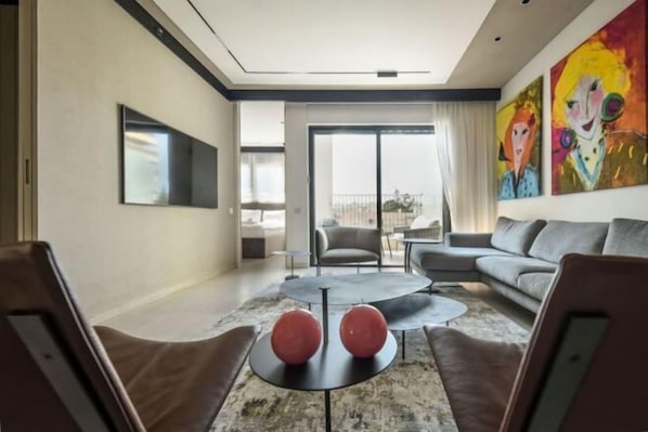 A modern living room with a large flat-screen TV, a sofa, a coffee table with two red spherical objects, and a colorful abstract painting on the wall.