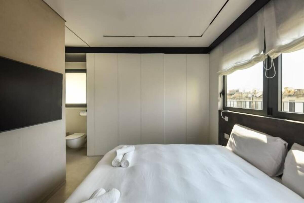 A modern hotel room with a large bed, a view of the city through the window, and a separate bathroom area.