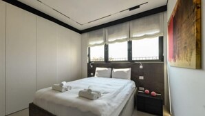 A modern bedroom with a large bed, a nightstand, and a window with sheer curtains. - Modern and Vibrant 1BR apt with Private Balcony (Tel Aviv)