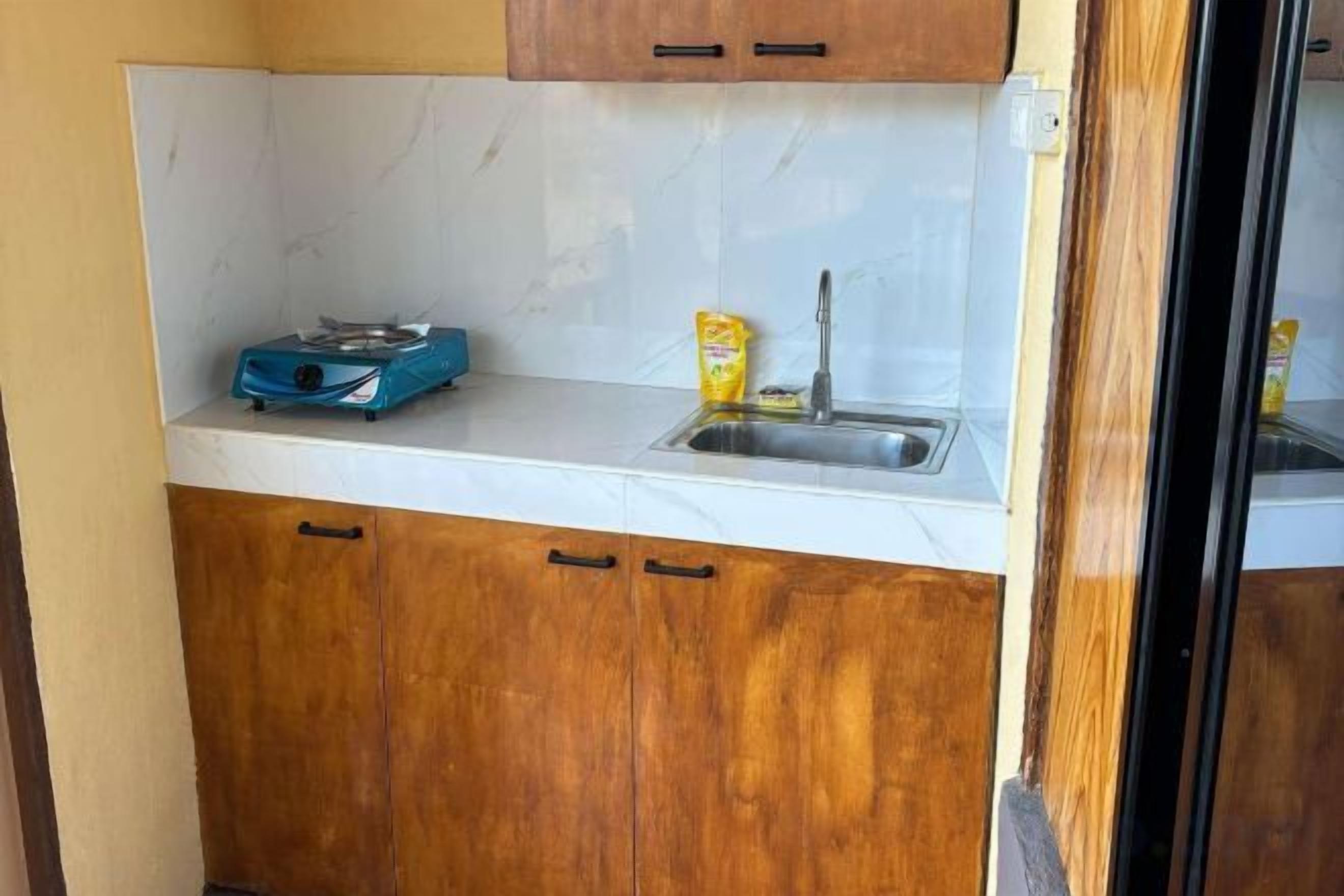 A compact kitchen with a white countertop, wooden cabinets, a blue scale, and a yellow container.