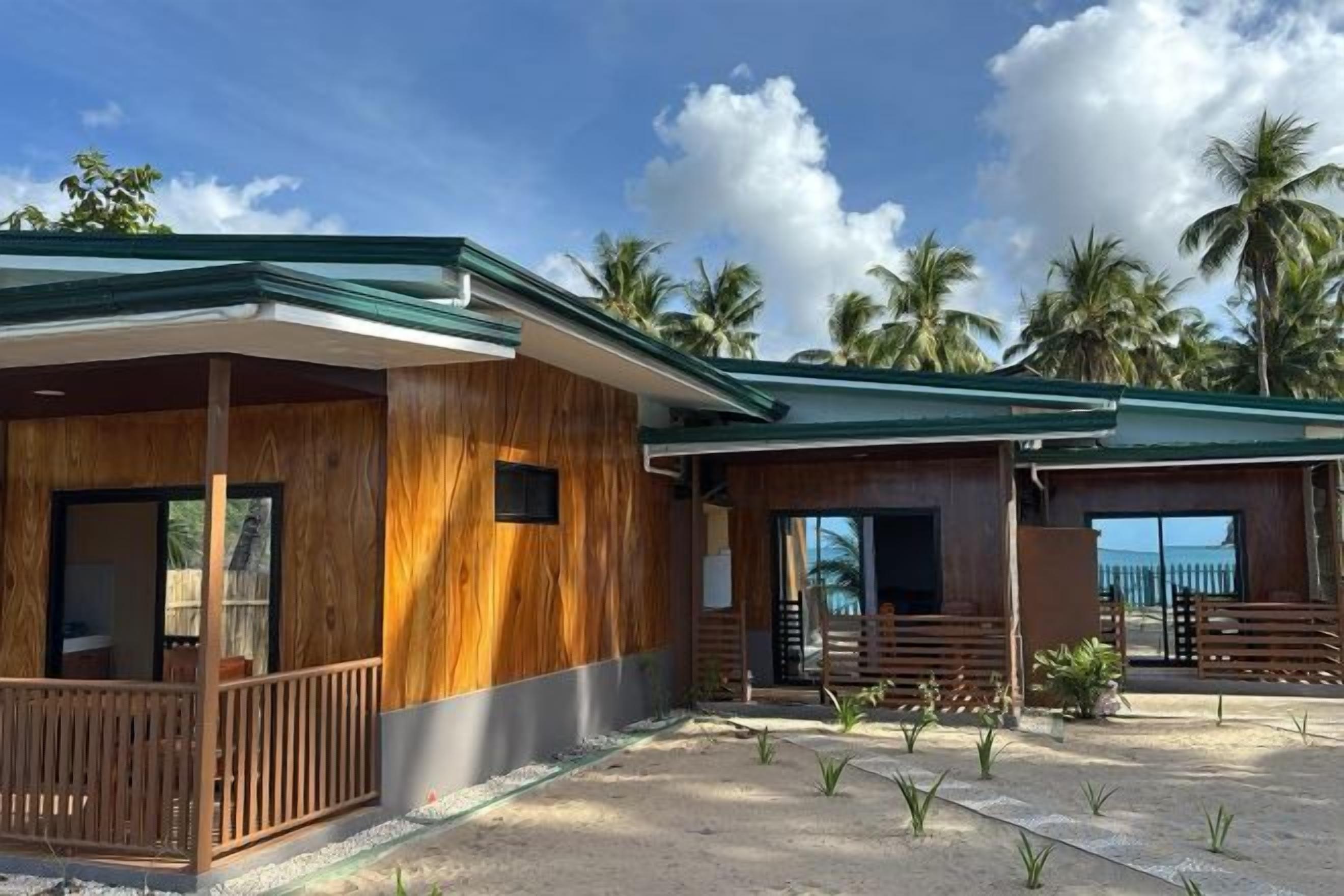 A two-story wooden building with a covered porch, large windows, and a view of palm trees.