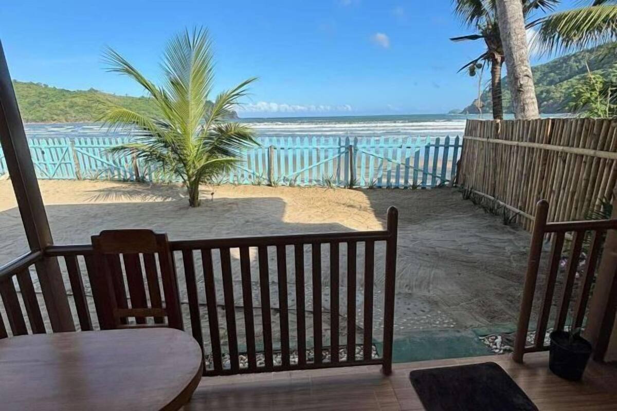 Uitzicht op een strand met een houten hek, een palmboom en een tafel.